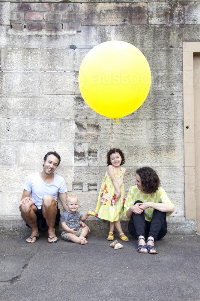 Portrait of a young family of four with a large yellow balloon - Australian Stock Image