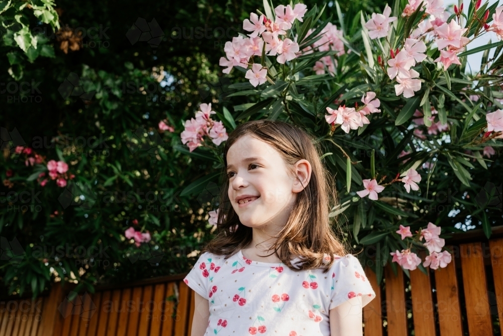 Portrait of a young girl outdoors in the afternoon in front of a timber fence and garden - Australian Stock Image