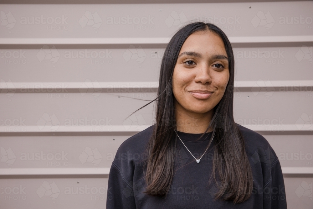 Portrait of a young, smiling,  first nations woman against wall outside - Australian Stock Image