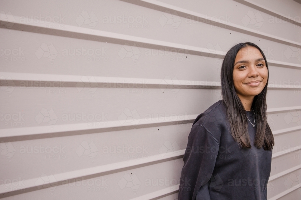 Portrait of a young, smiling,  first nations woman against wall outside - Australian Stock Image