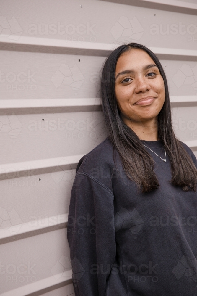 Portrait of a young, smiling,  first nations woman against wall outside - Australian Stock Image