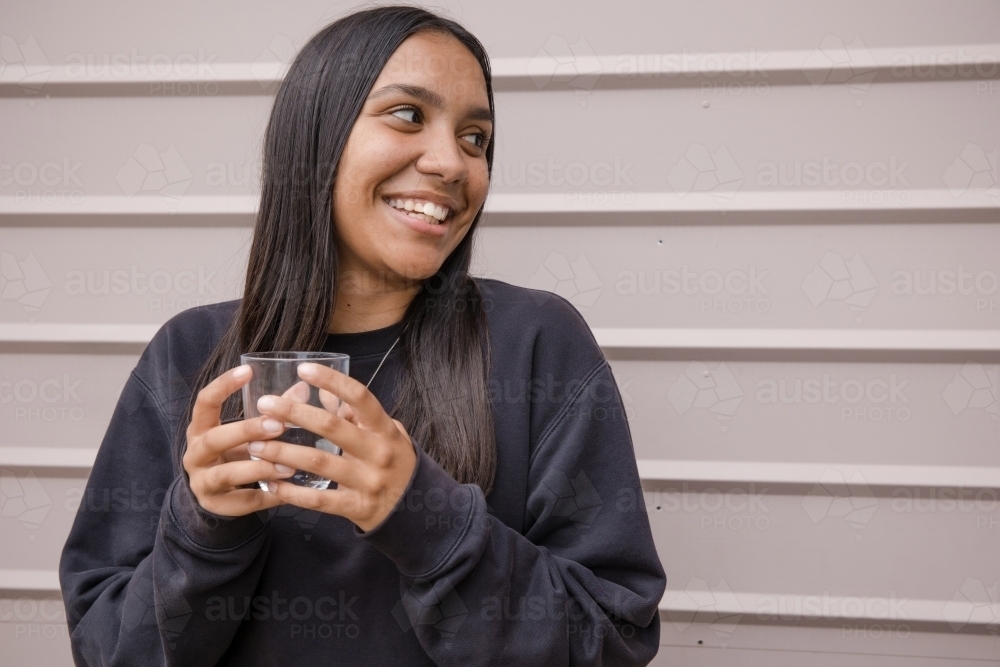 Portrait of a young, smiling, first nations woman holding a glass of water - Australian Stock Image