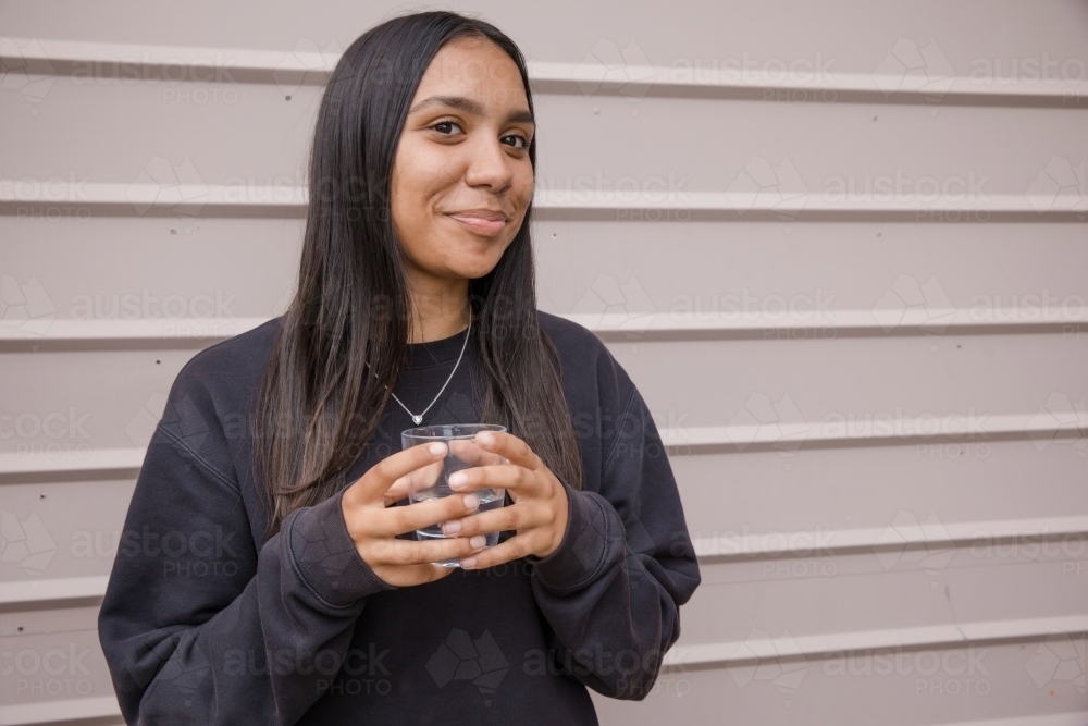 Portrait of a young, smiling, first nations woman holding  a glass of water - Australian Stock Image