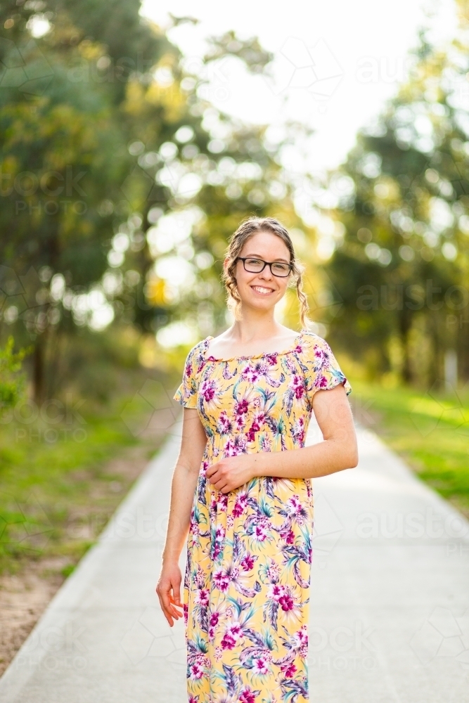 Portrait of a young woman with glasses standing on a pedestrian foot path through a park - Australian Stock Image