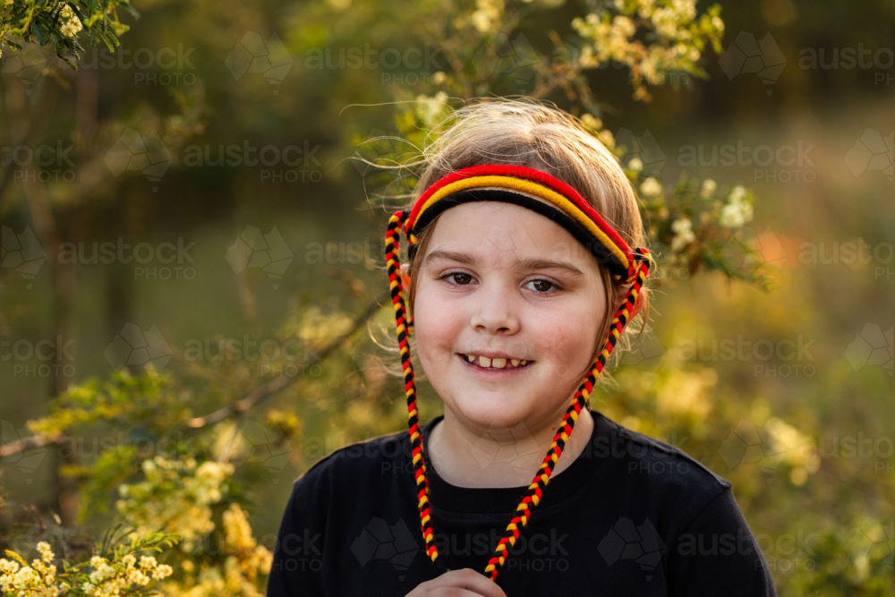 Portrait of Aboriginal little girl with red yellow and black headband in Australian bushland - Australian Stock Image