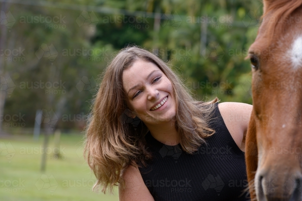 Portrait of an attractive young woman with long brown hair and a chestnut horse - Australian Stock Image