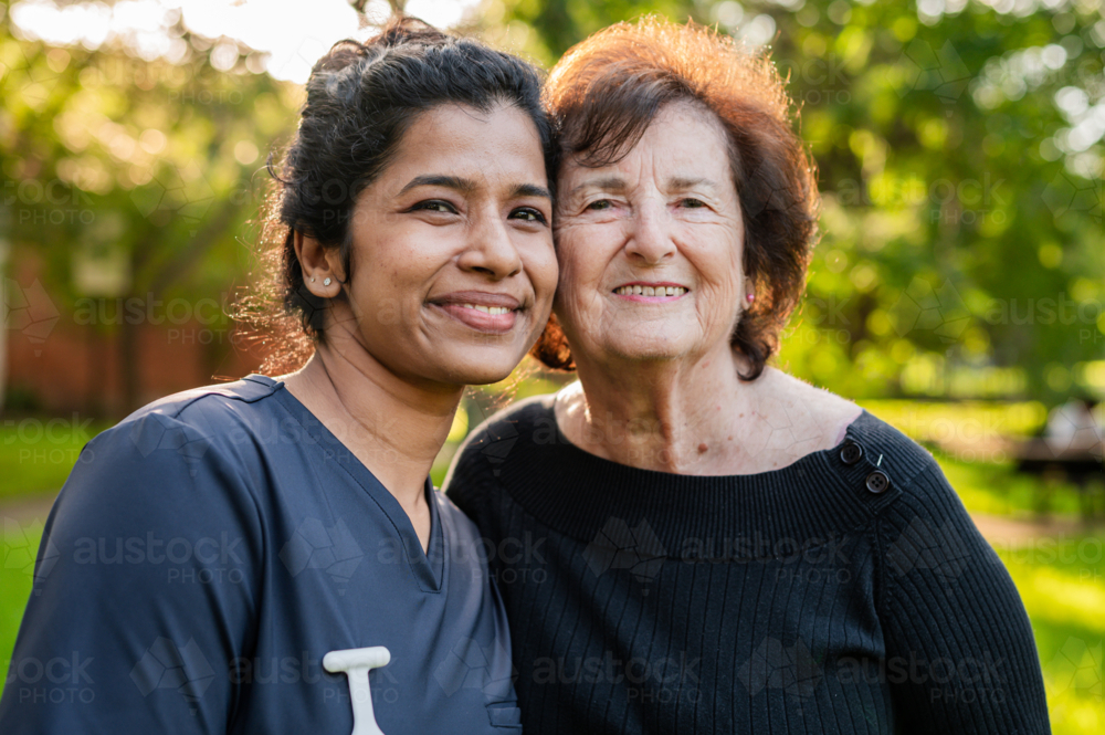 Portrait of an elderly woman and healthcare worker standing outdoors on a sunlit garden - Australian Stock Image
