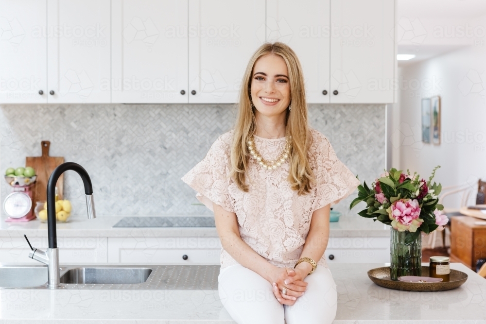 Portrait of an interior designer sitting on a kitchen bench - Australian Stock Image
