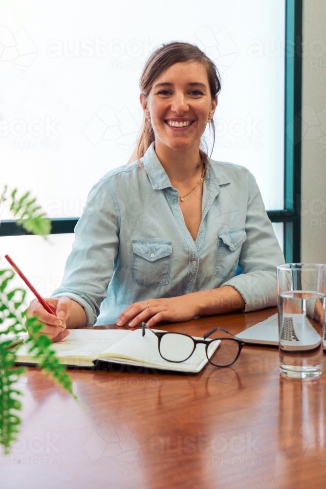 Portrait of an office worker sitting with laptop and note book at a meeting table - Australian Stock Image