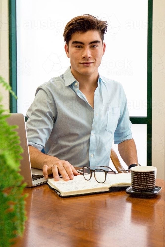 Portrait of an office worker sitting with laptop and note book at a meeting table - Australian Stock Image