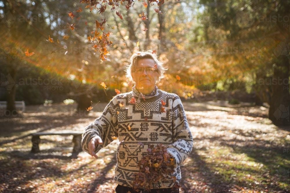 Portrait of an older man throwing autumn leaves in the park - Australian Stock Image