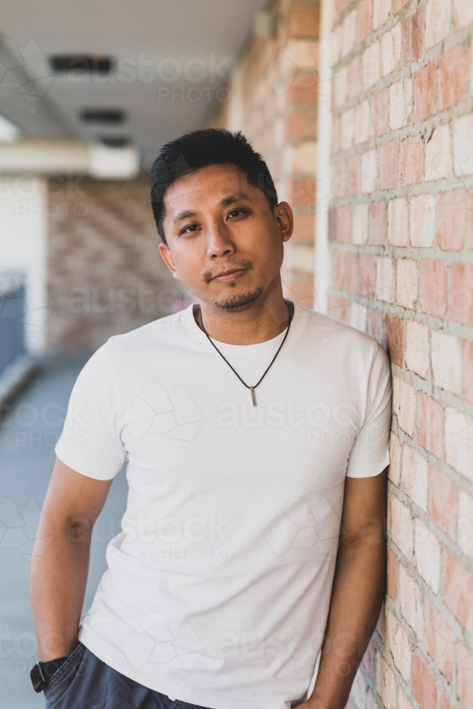 portrait of asian man leaning against brick wall - Australian Stock Image