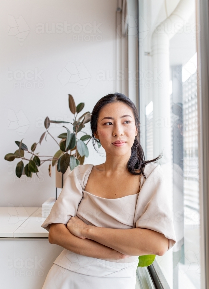 Image of Asian woman standing by the window in an office - Austockphoto