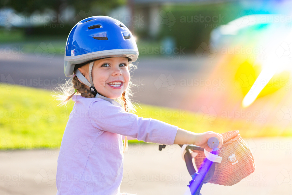 Portrait of Australian child and rainbow light over girl riding bike in blue helmet - Australian Stock Image