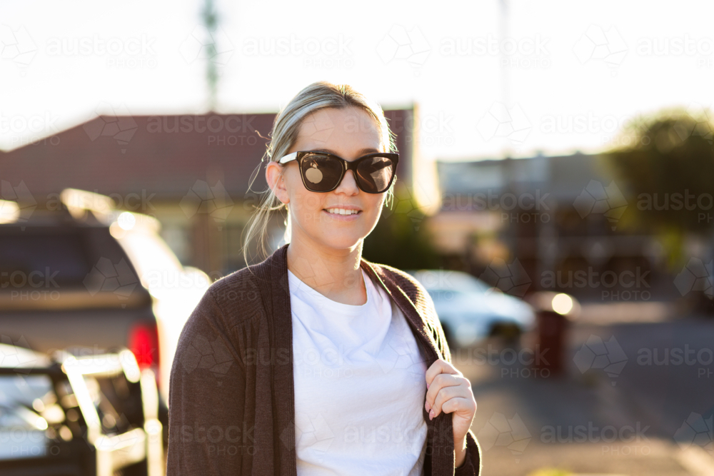 Portrait of backlit twentysomething First Nations Australian woman with sunglasses by urban street - Australian Stock Image
