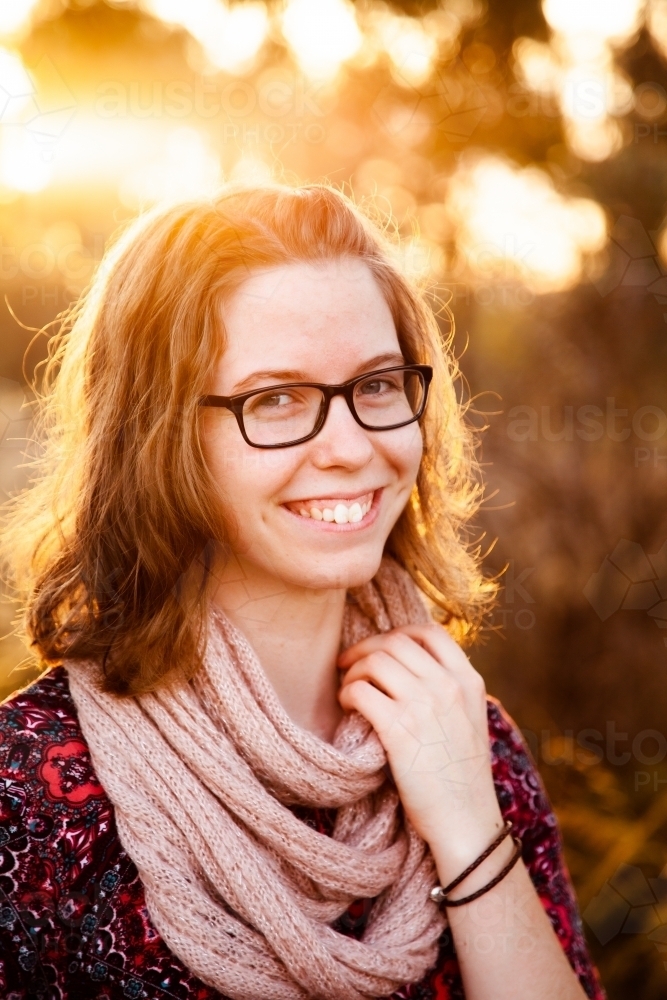 Portrait of backlit young woman smiling outside wearing scarf in winter - Australian Stock Image