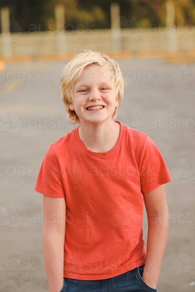 Portrait of caucasian boy with blonde hair with big smile wearing orange shirt - Australian Stock Image