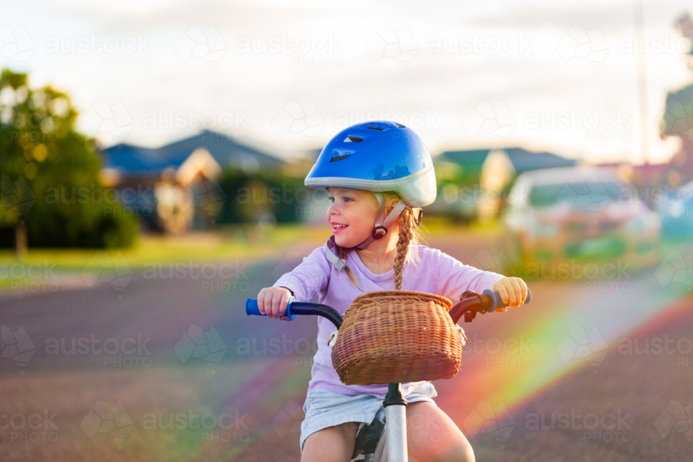 Portrait of child and rainbow light over girl riding bike on quiet urban street - Australian Stock Image