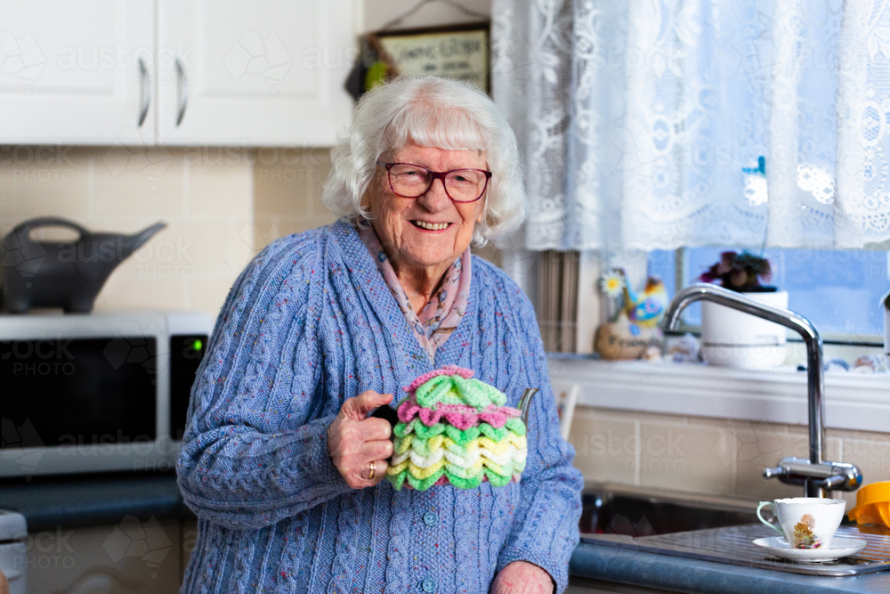 Portrait of elderly Australian woman inside her home holding teapot in crochet tea cosy - Australian Stock Image
