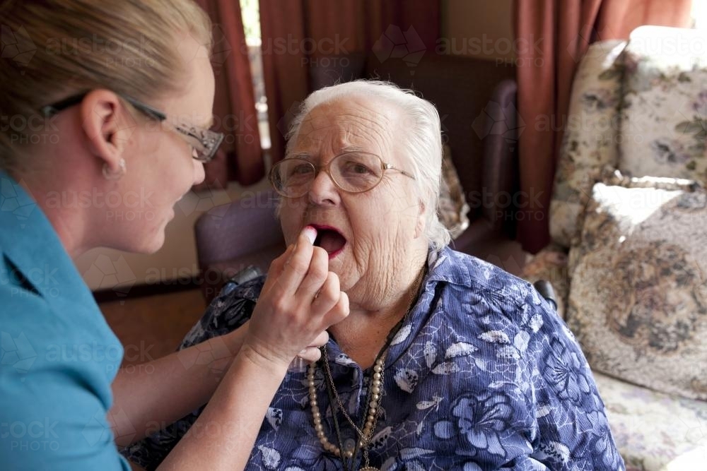 Portrait of elderly lady having lipstick applied by carer at aged care facility - Australian Stock Image