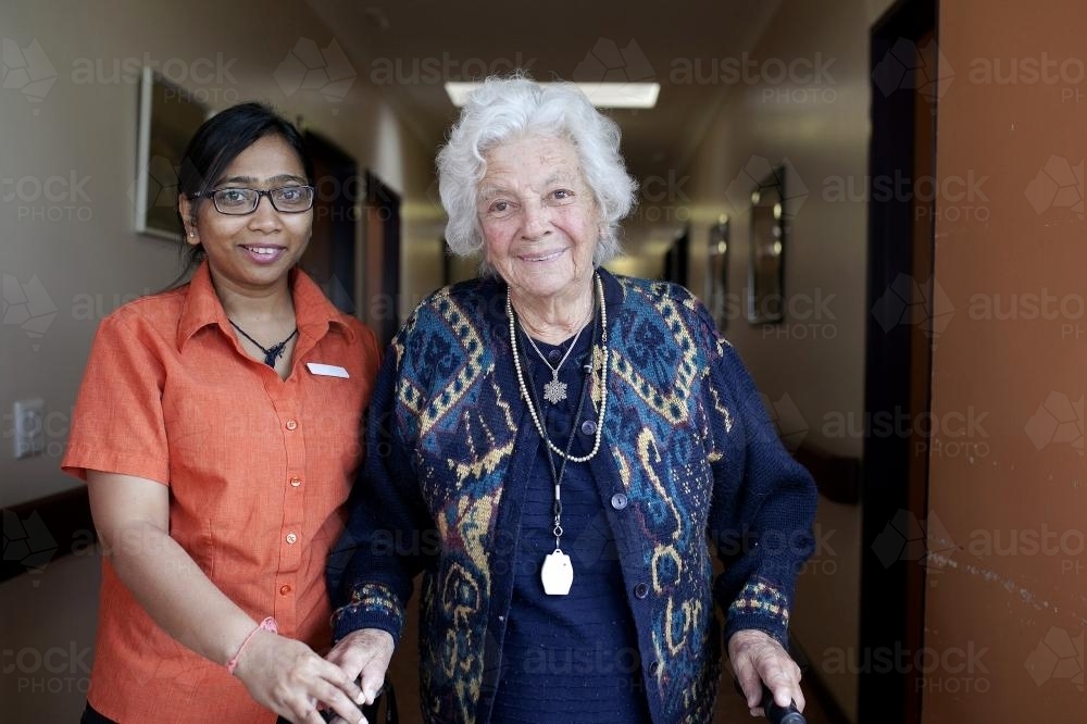Portrait of elderly lady walking with carer at aged care facility - Australian Stock Image