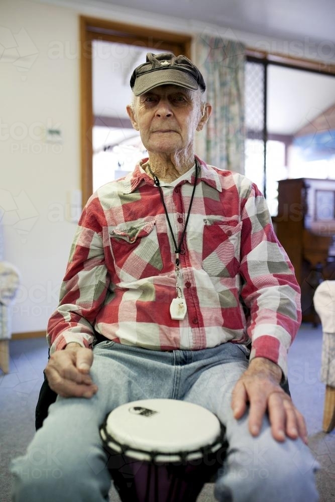Portrait of elderly man during bongo drumming session at retirement village - Australian Stock Image