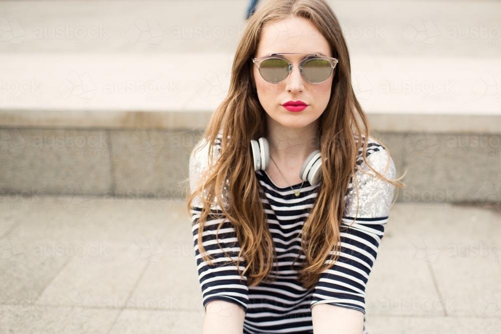Portrait of fashionable young woman wearing sunglasses sitting down - Australian Stock Image