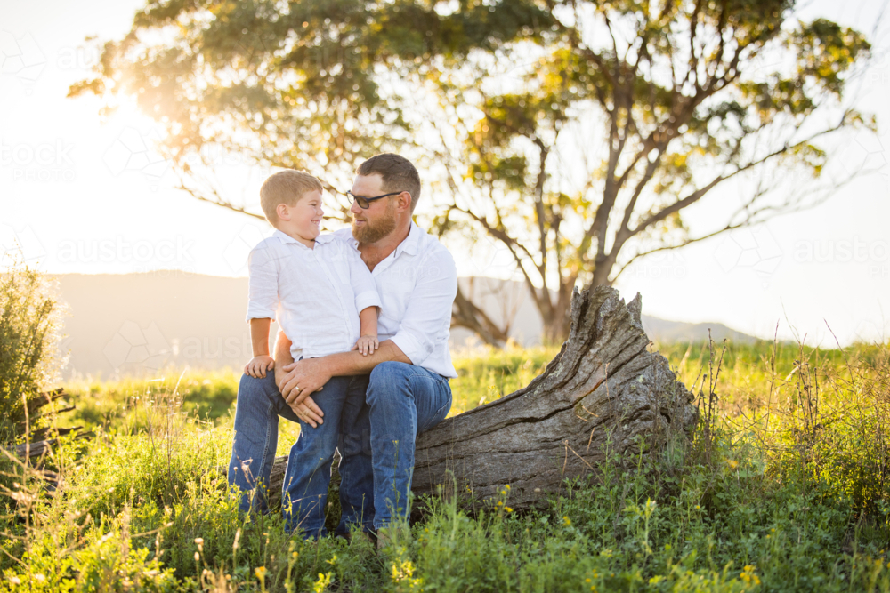 Image of Portrait of father and son sitting together on log on ...