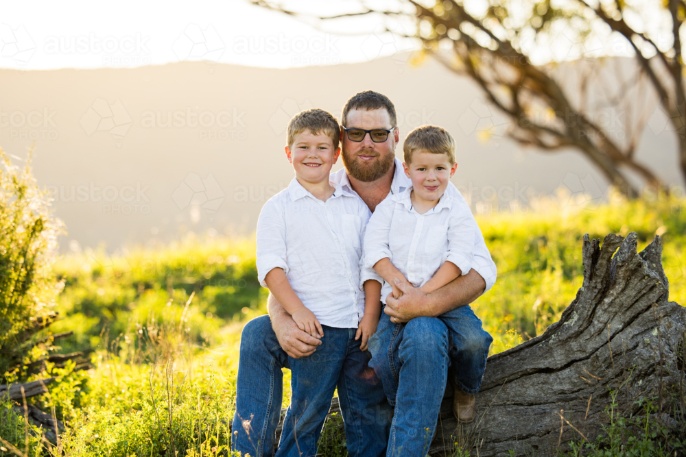 Image of Portrait of father and sons sitting together on log on ...