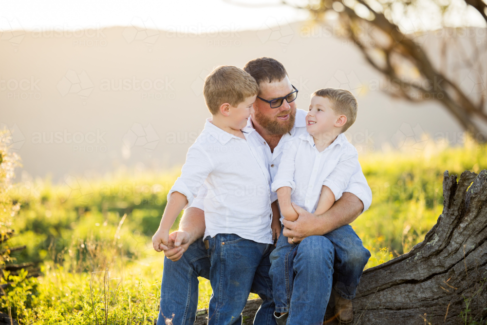 Image of Portrait of father and sons sitting together on log on ...