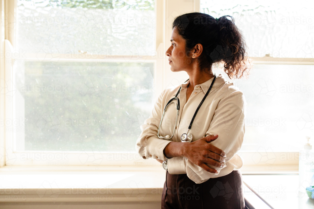Portrait of female medical practitioner standing beside a softly lit window inside the clinic - Australian Stock Image