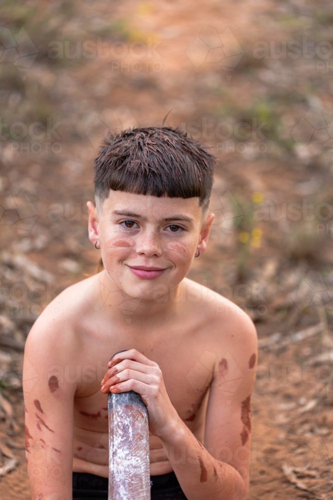 Portrait of First Nations Australian kid holding didgeridoo with brown ochre body paint - Australian Stock Image