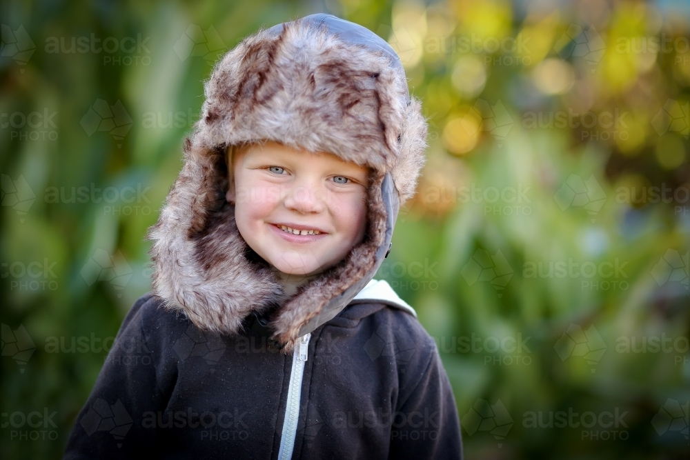 Portrait of happy 3 year old boy wearing warm hat outdoors on cold winter day - Australian Stock Image