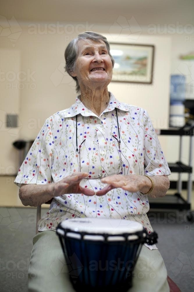 Portrait of happy elderly lady during bongo drumming session at retirement village - Australian Stock Image