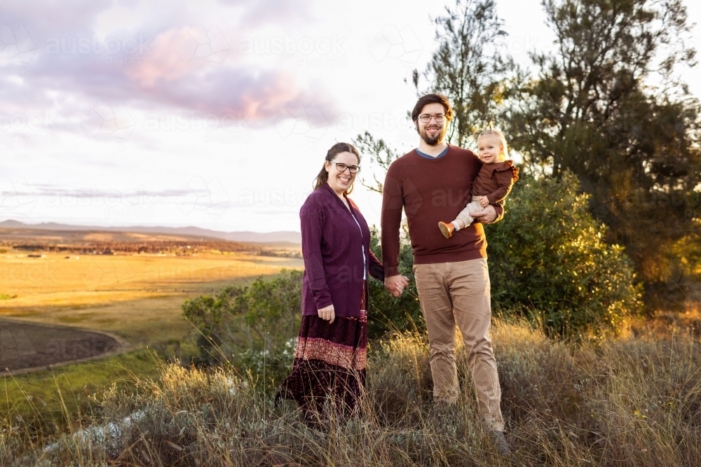 Portrait of happy family standing together on cliff in paddock at sunset - Australian Stock Image