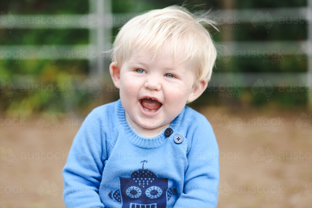 Portrait of happy little toddler boy sitting in garden smiling - Australian Stock Image