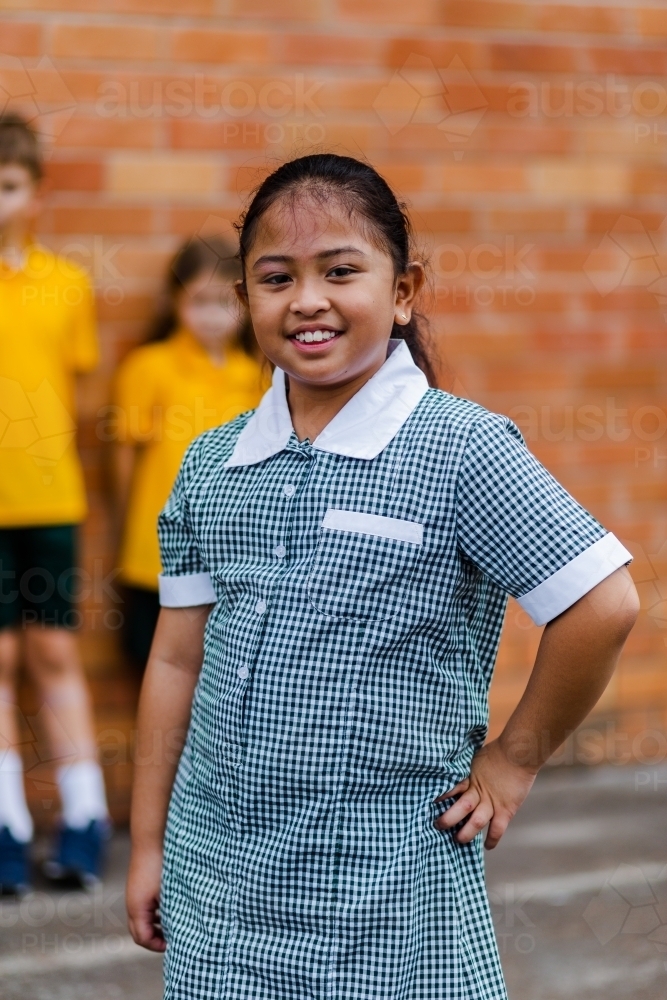 Portrait of happy young Aussie school girl of Filipino ethnicity smiling and wearing a dress - Australian Stock Image