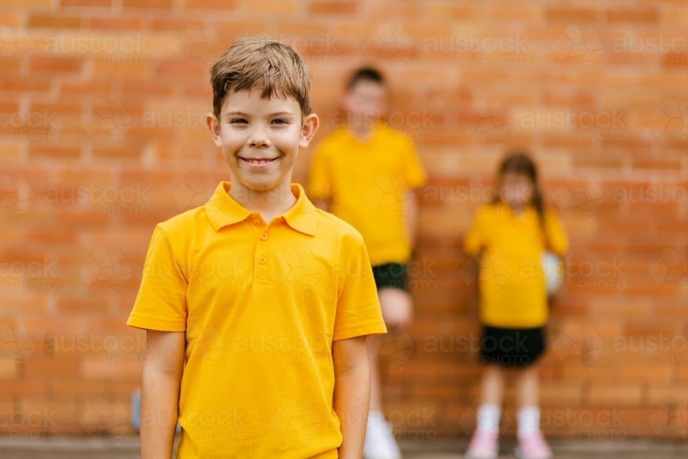 Portrait of happy young school boy at Aussie public school in yellow uniform - Australian Stock Image