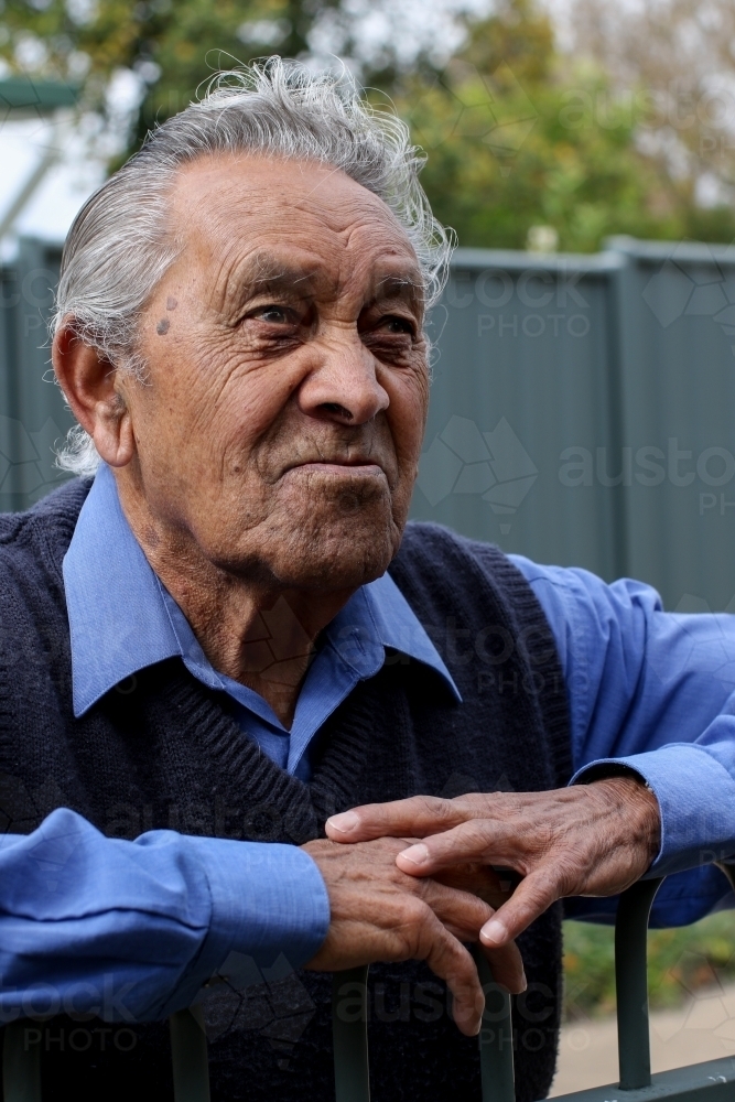 Portrait of male Aboriginal elder looking upwards while leaning on a fence - Australian Stock Image