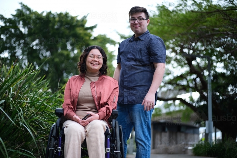 Portrait of man standing and a woman with a disability in a wheel chair outside - Australian Stock Image