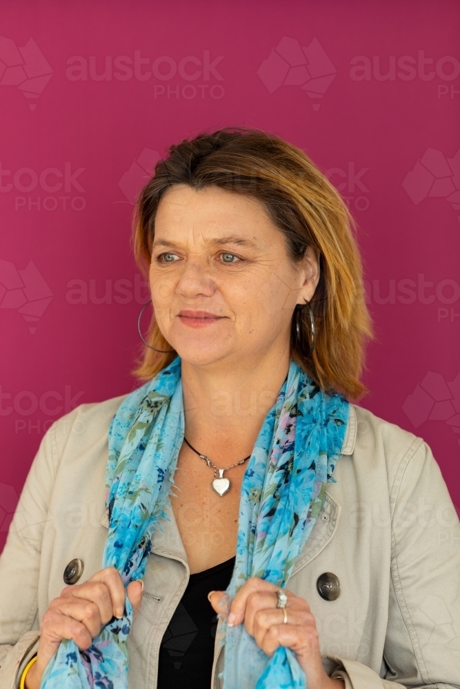 portrait of mature woman wearing blue scarf against dark pink background - Australian Stock Image
