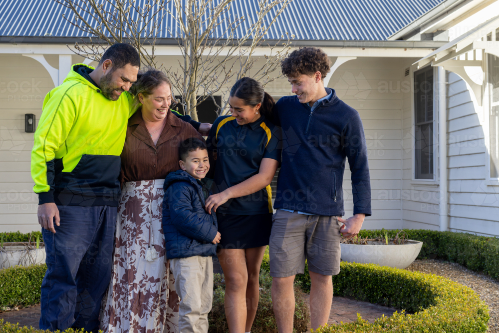 Portrait of mixed ethnicity family standing on brick pathway in front of white house - Australian Stock Image