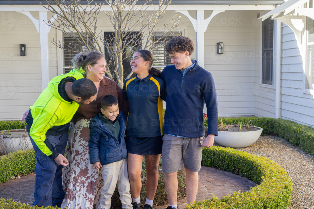 Portrait of mixed ethnicity family standing on brick pathway in front of white house - Australian Stock Image