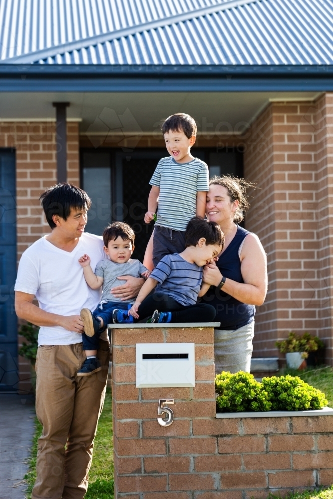 portrait of mixed race Chinese Australian family outside home with kids sitting on mailbox - Australian Stock Image
