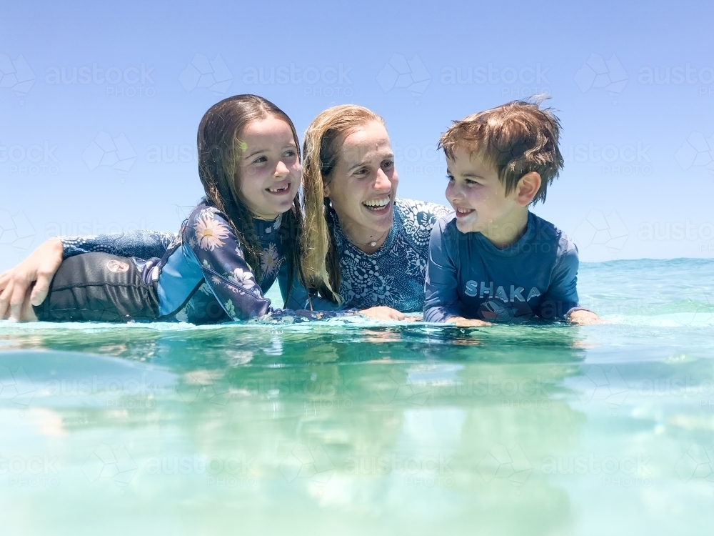 Portrait of Mother and two children in ocean leaning on surfboard - Australian Stock Image
