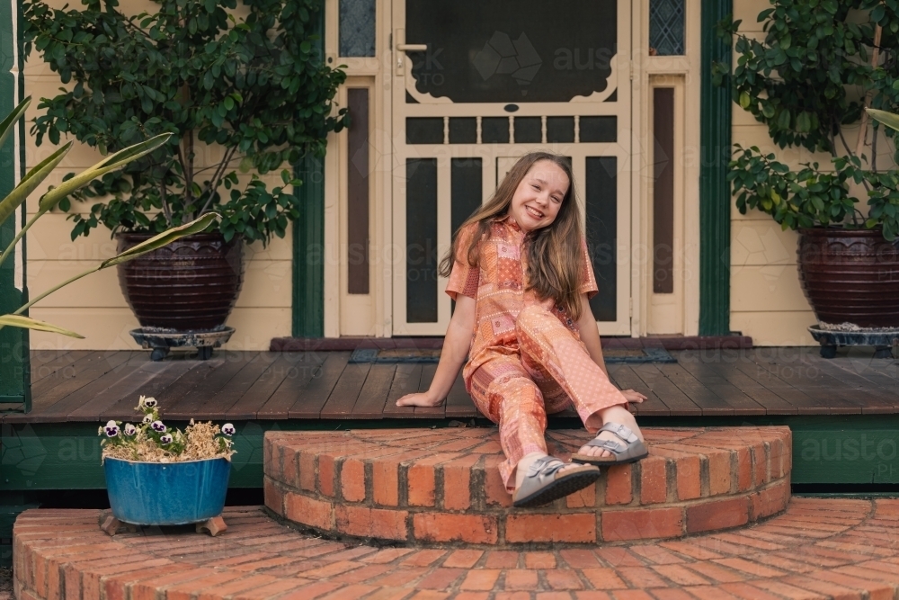 Portrait of pre-teen girl sitting on front verandah of country house - Australian Stock Image