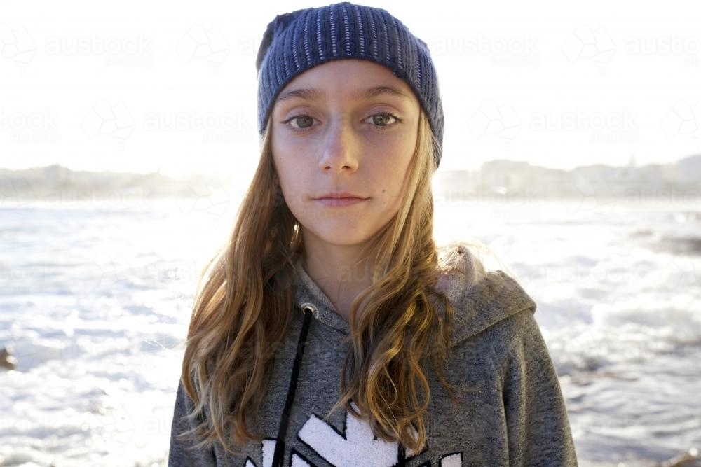 Portrait of pre teen girl with beanie on looking into camera by the ocean - Australian Stock Image