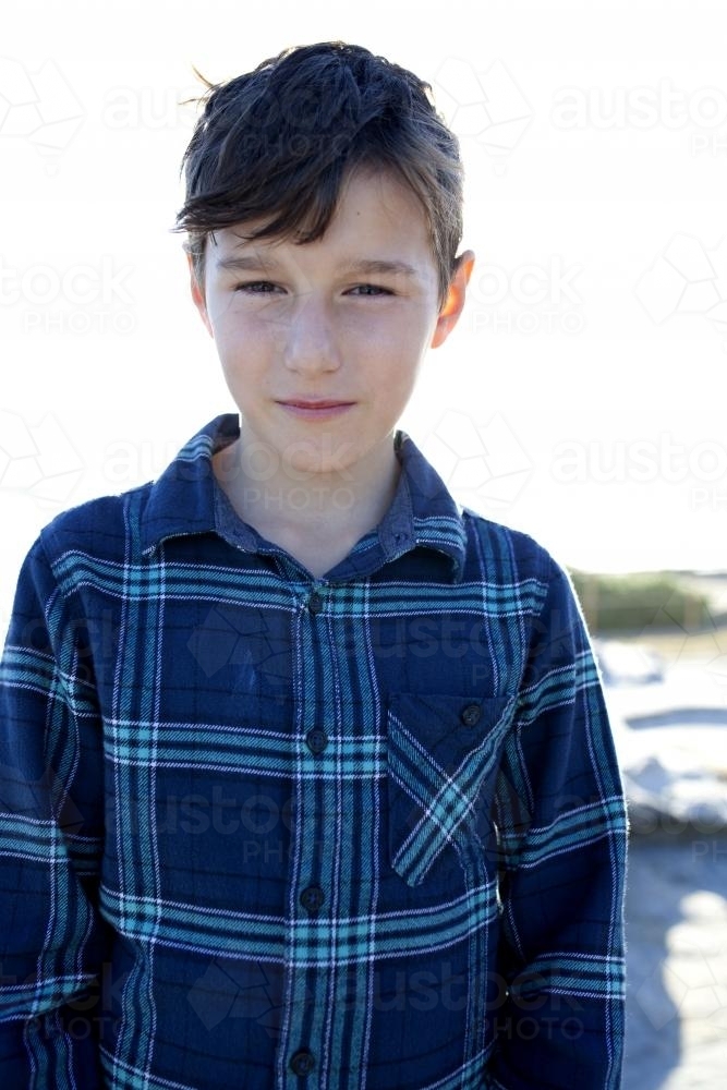 Portrait of serious boy looking at camera with afternoon light behind - Australian Stock Image