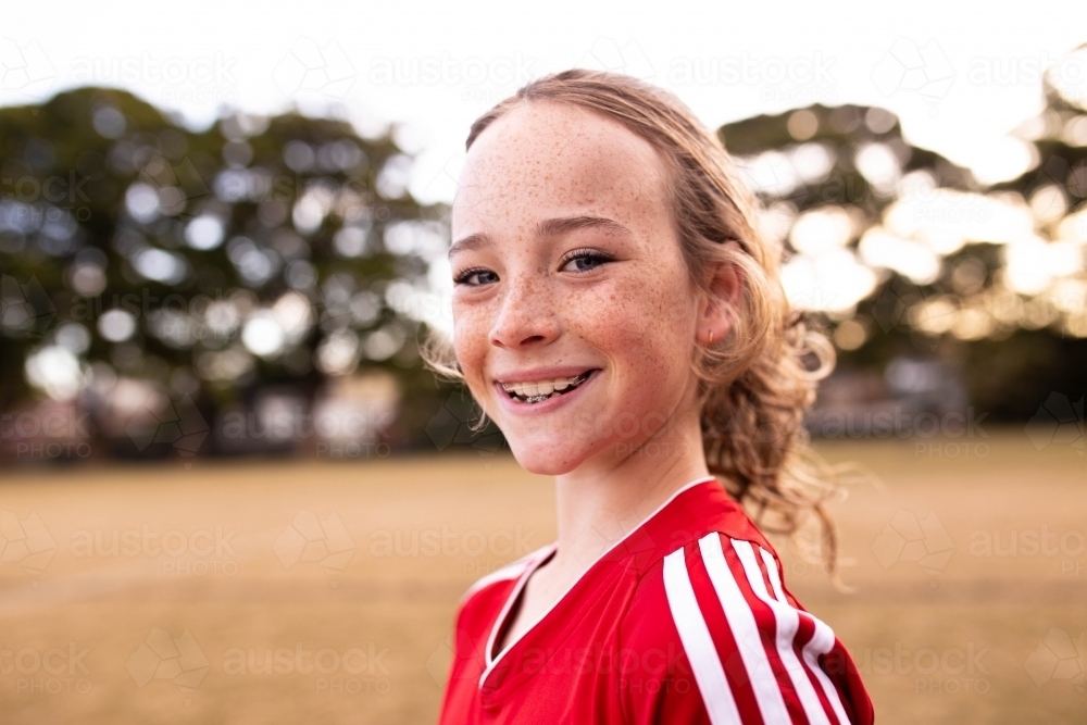 Portrait of single tween girl football player wearing a red sports uniform - Australian Stock Image