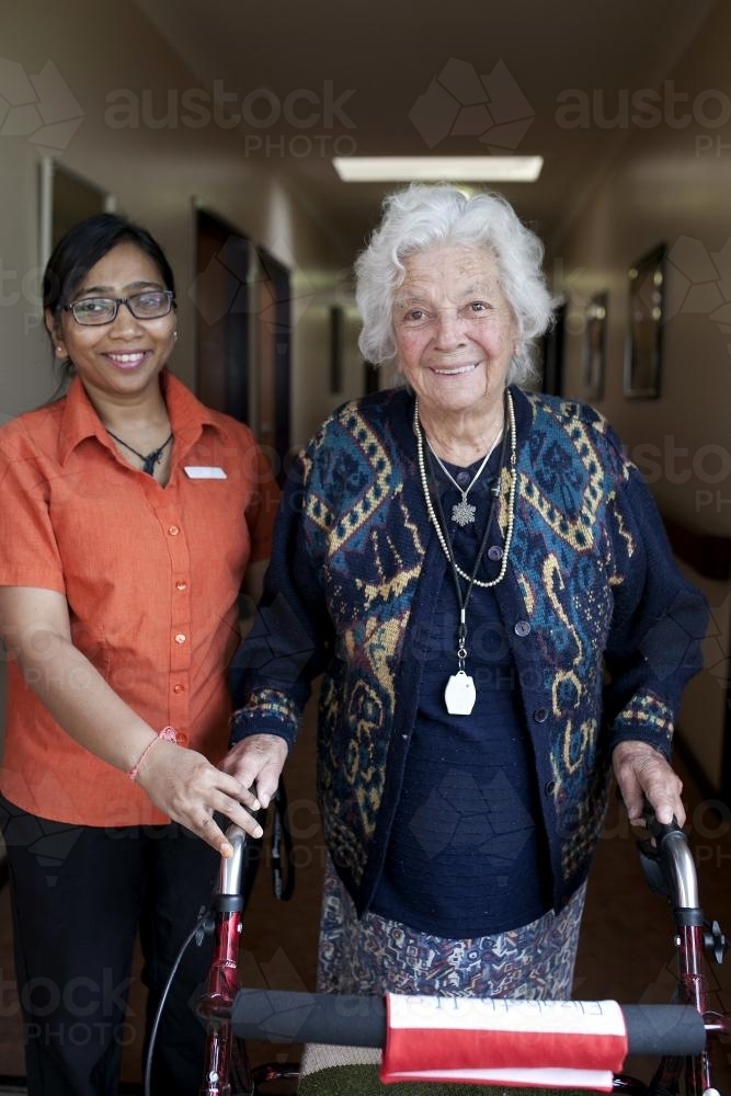 Portrait of smiling elderly lady walking with carer at aged care facility - Australian Stock Image
